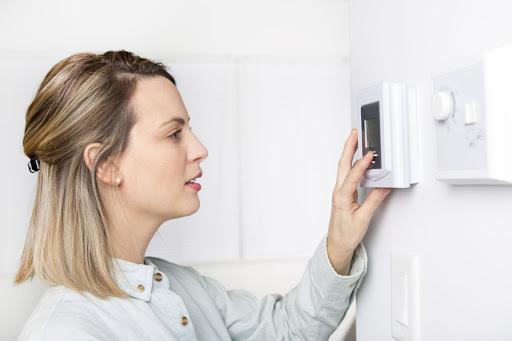 A woman adjusting a thermostat in a home.