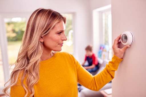 Woman adjusting thermostat inside home