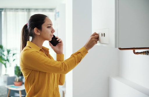 A woman on the phone while looking at a boiler in a home.