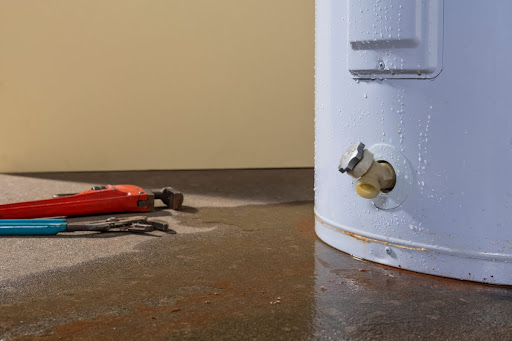 A water heater with tools and a puddle of water around it.