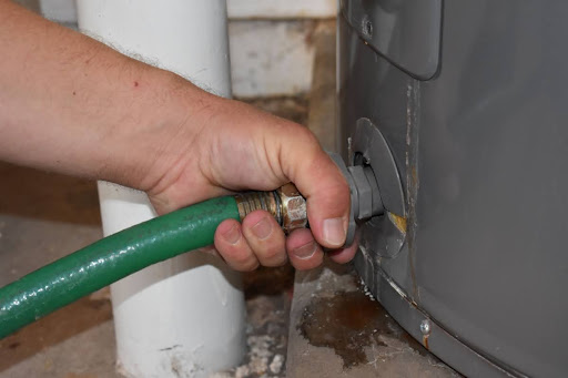 A hand attaching a hose to a water heater drain valve.