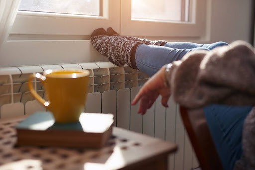 Woman resting feet on radiator with a hot mug on the table next to her.